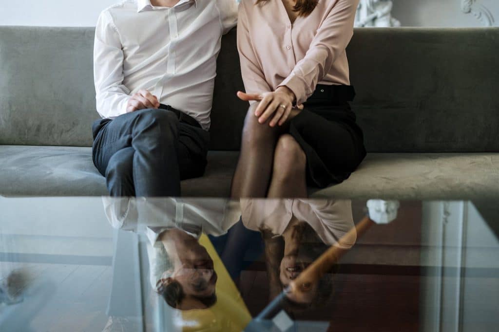 A couple sitting on a sofa, reflecting on glass table during consultation.